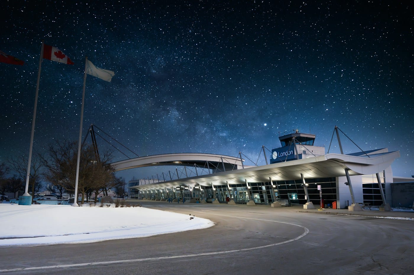 A small airport terminal glowing under a night sky full of stars, Canadian flags flying beside it.