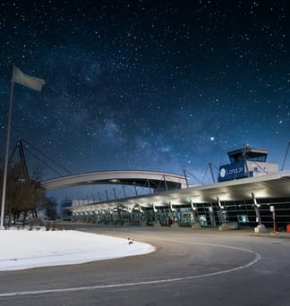A small airport terminal glowing under a night sky full of stars, Canadian flags flying beside it.