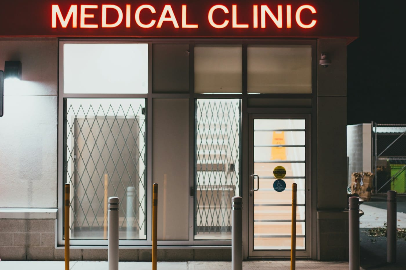 The entrance of a medical clinic at night, a red neon “Medical Clinic” sign above lit glass doors.