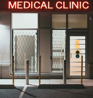 The entrance of a medical clinic at night, a red neon “Medical Clinic” sign above lit glass doors.